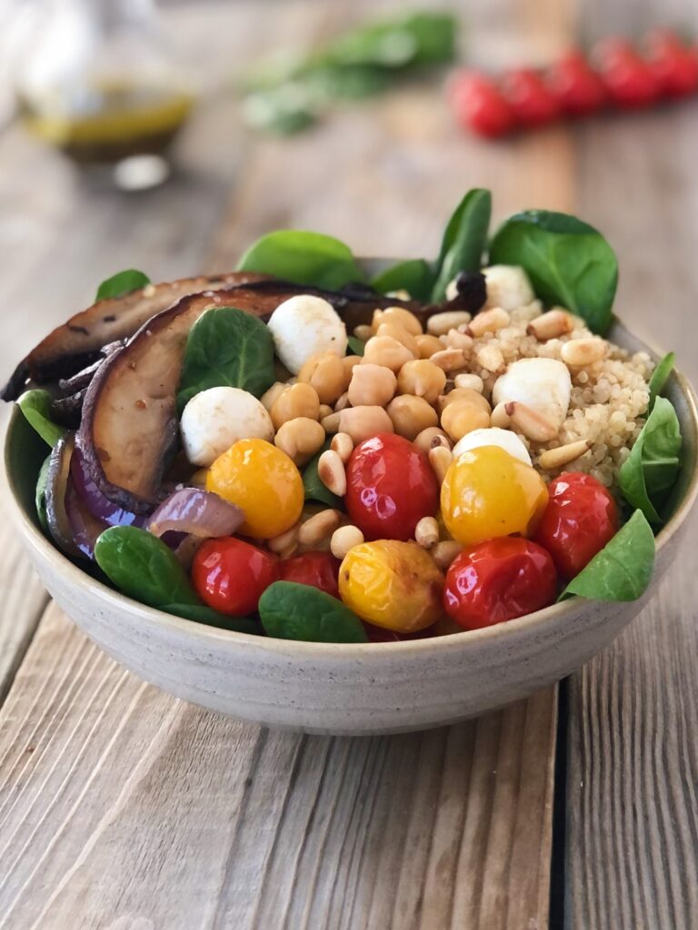 Quinoa veggie bowl on a table with dressing in a jug behind it.