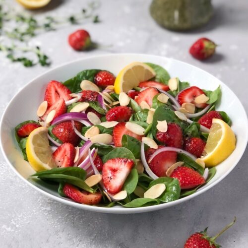 Square image of Spinach strawberry salad garnished with lemons.