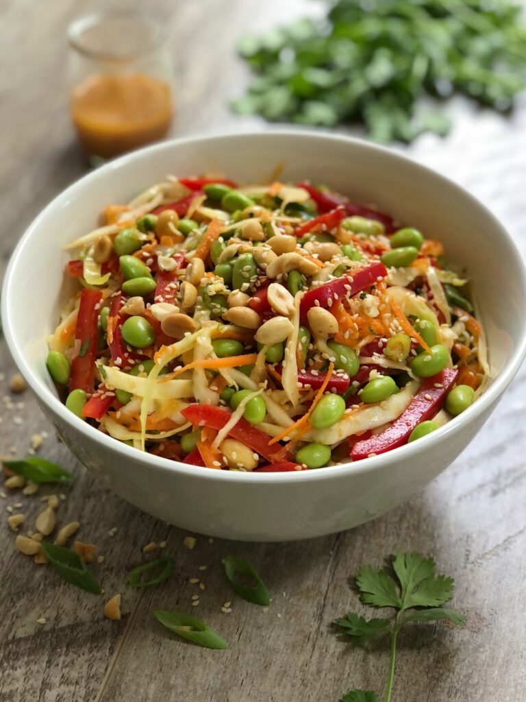 Edamame salad in a white bowl on a table with miso dressing on the side.