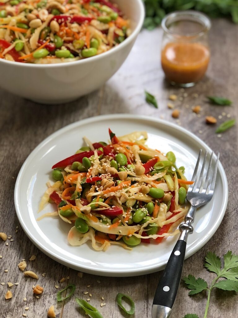 Edamame slaw serving on a white plate with sesame miso dressing in a jar.