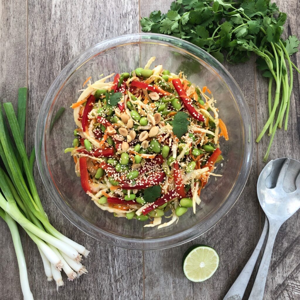 Edamame salad tossed together with garnishes in a glass bowl.