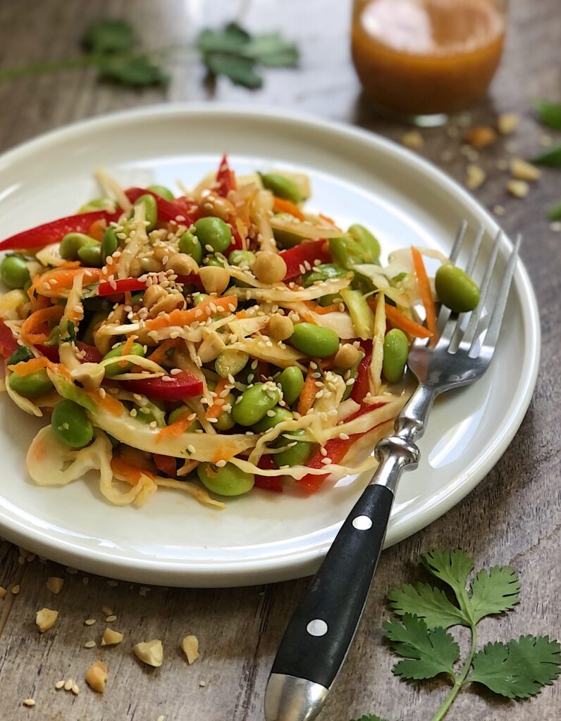 Serving of cabbage and edamame slaw on a white plate with a fork.